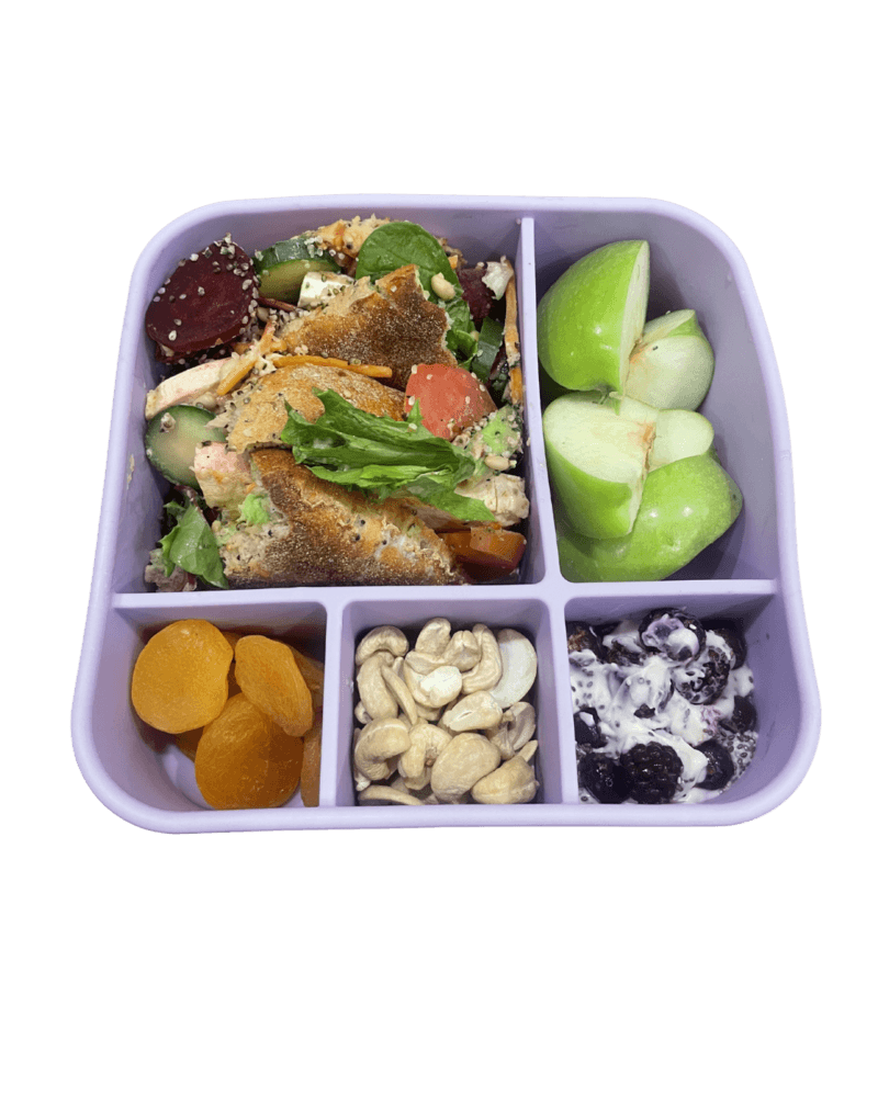 A bento-style lunch box with salad, fruits, and nuts